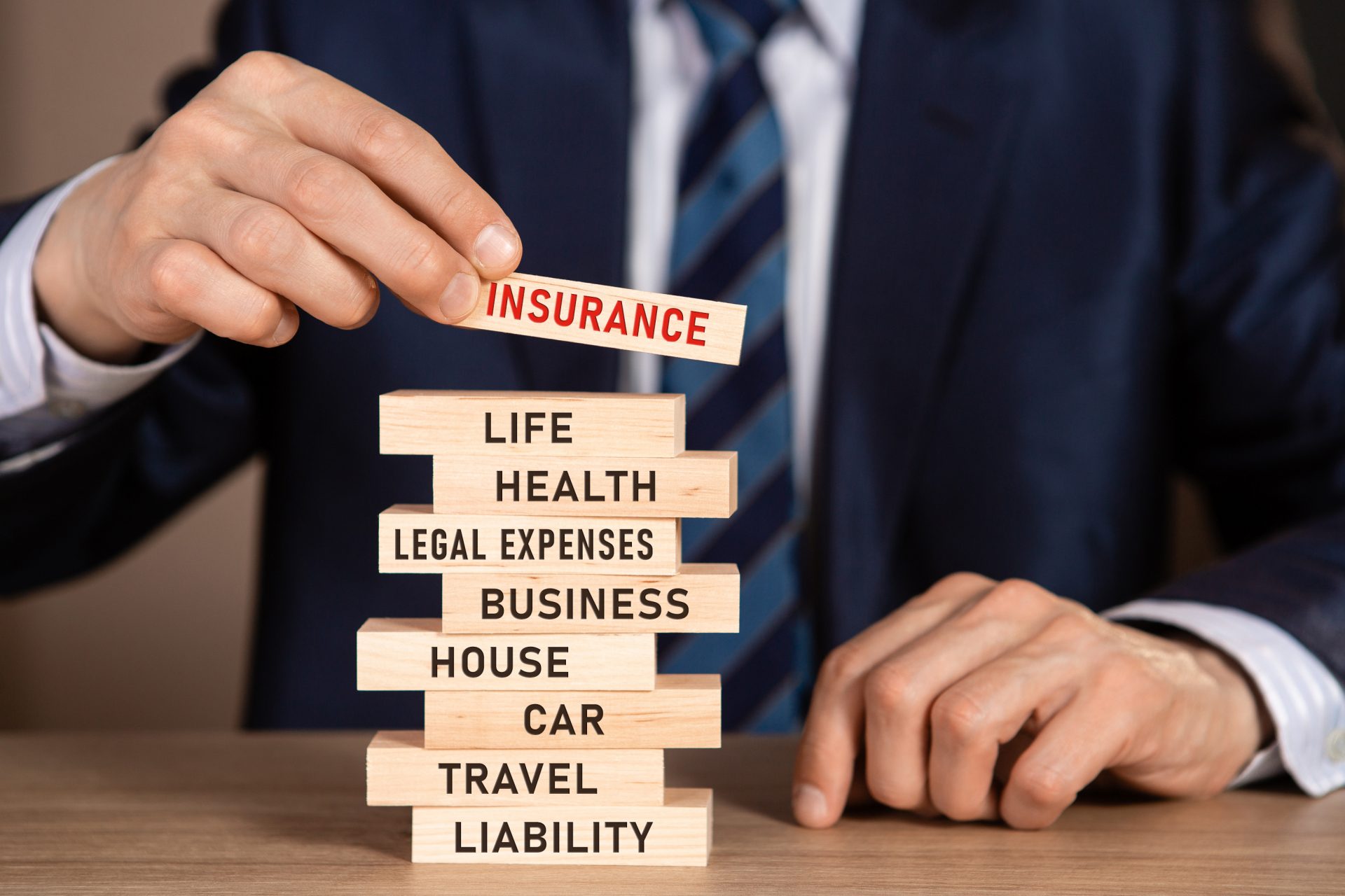  A person stacking wooden blocks with different types of monthly insurance premiums written on each block.